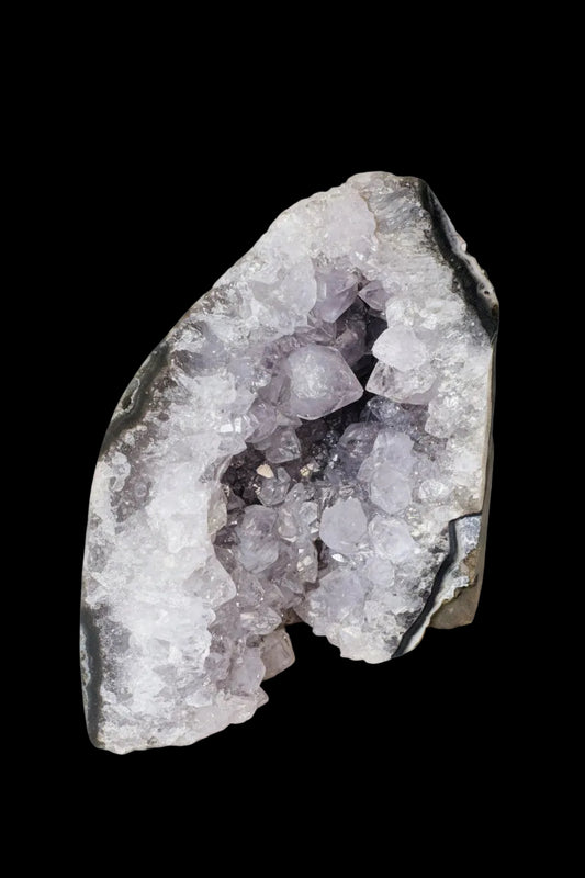 A raw amethyst geode specimen with light purple crystal clusters inside and a dark gray to black rough outer matrix, photographed on a solid white background.